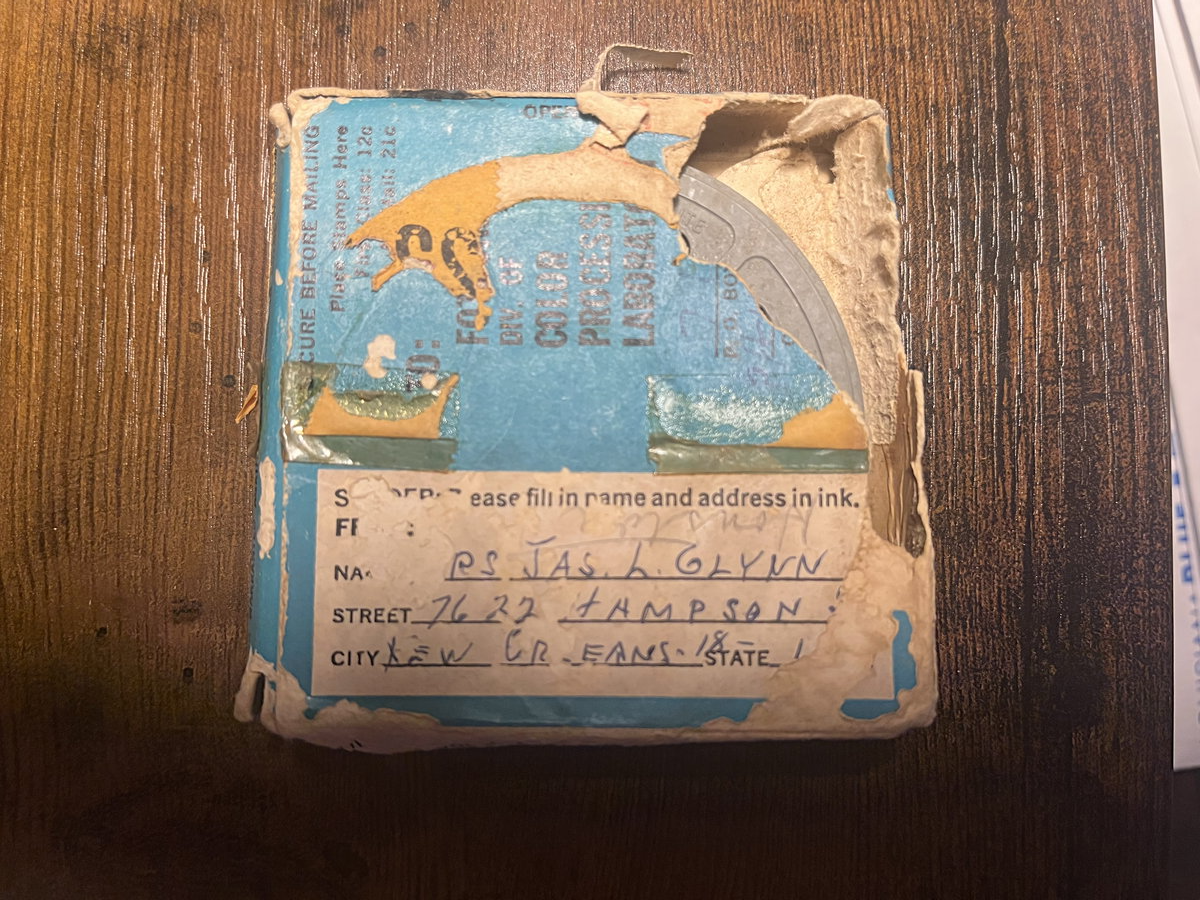 A worn blue-and-yellow Kodak processing mailer, flattened and creased, with a handwritten address, on a dark oak table.