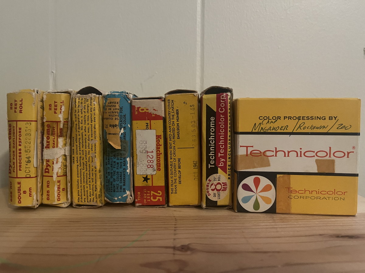 A row of yellow and red Kodak and Technicolor film processing boxes on a plywood shelf.