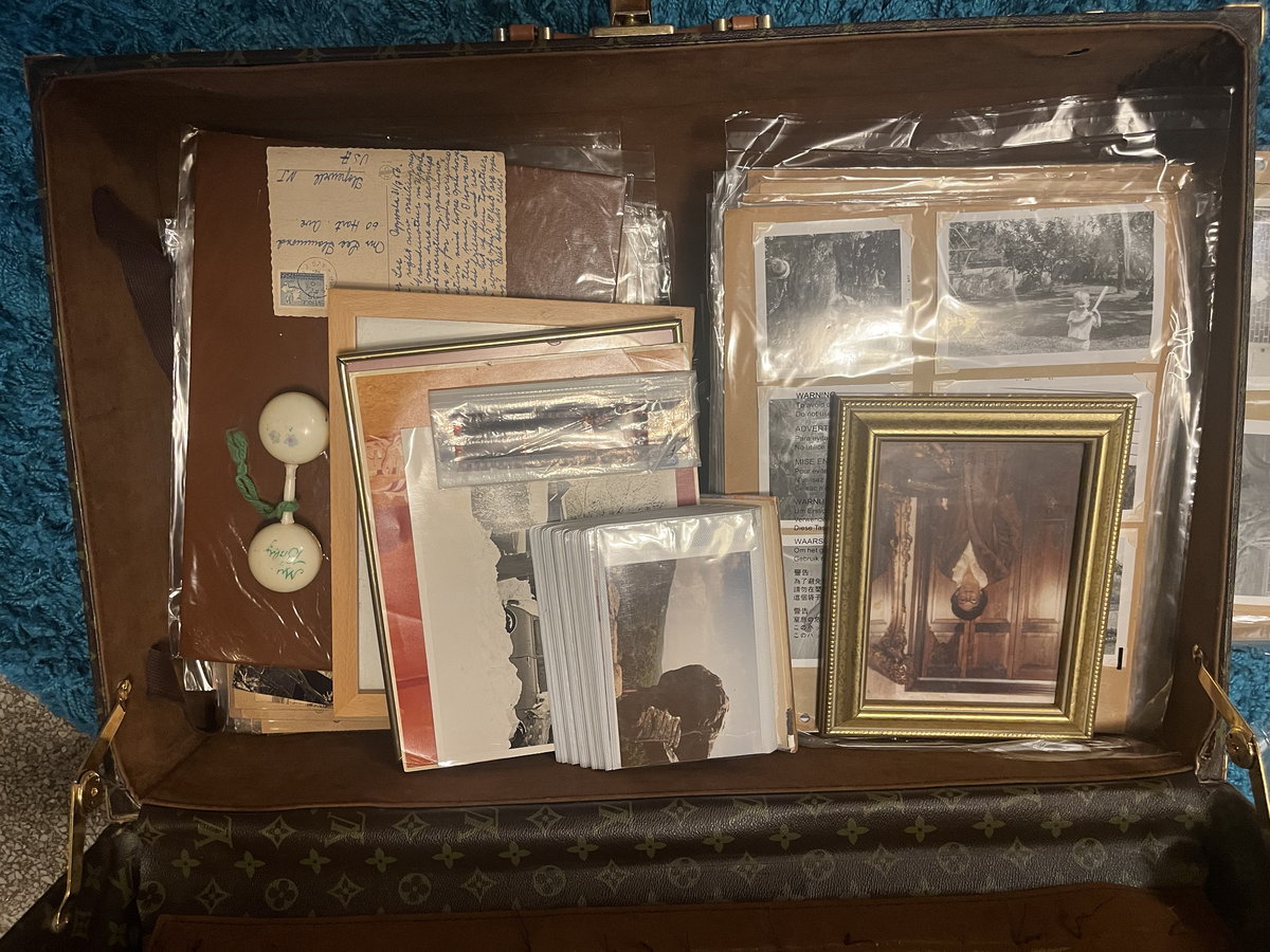 A suitcase holding sleeved photographs, a framed print, and papers.