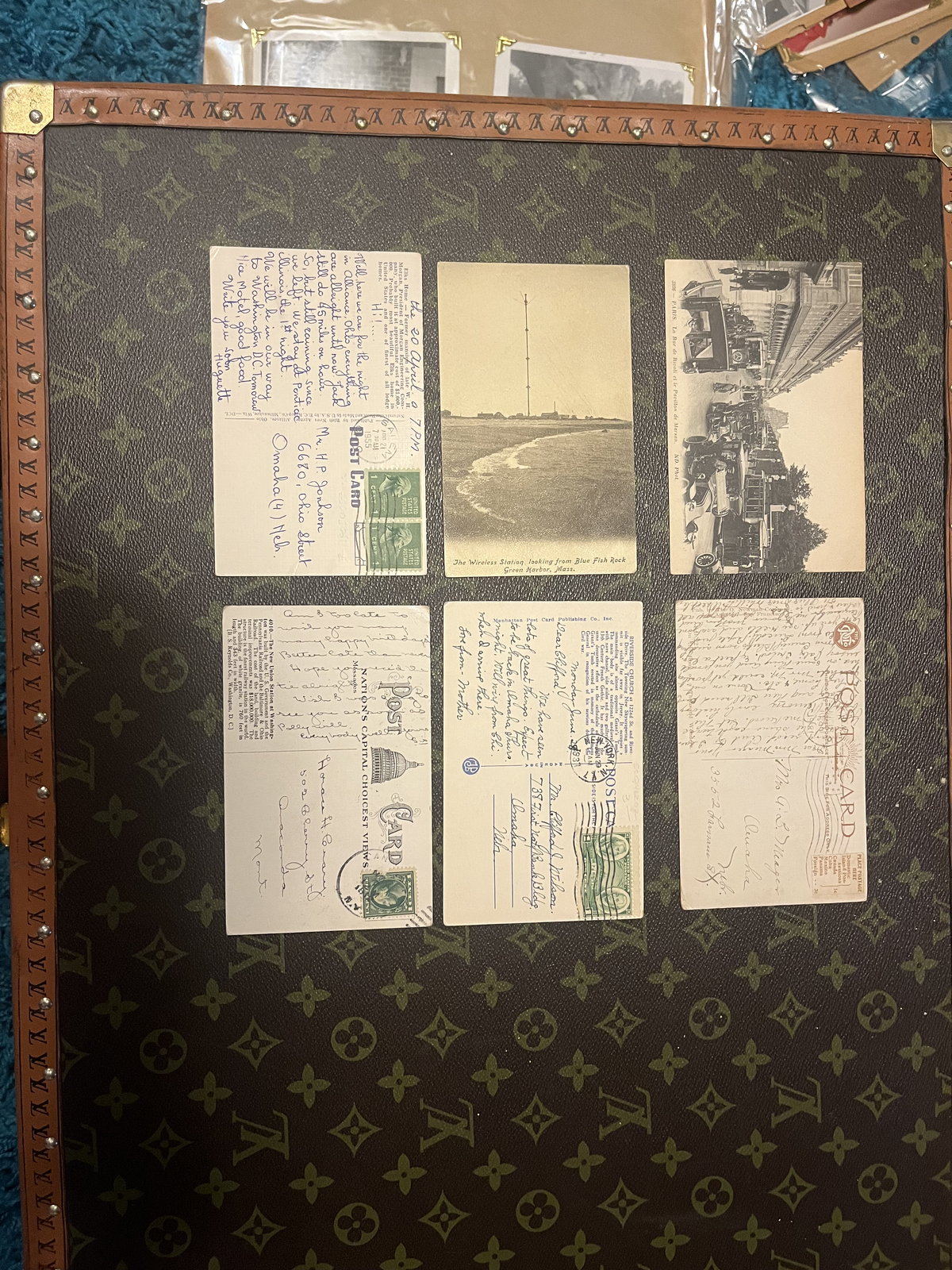 Vintage postcards laid out in a grid on top of a monogrammed leather case, waiting to be sorted.