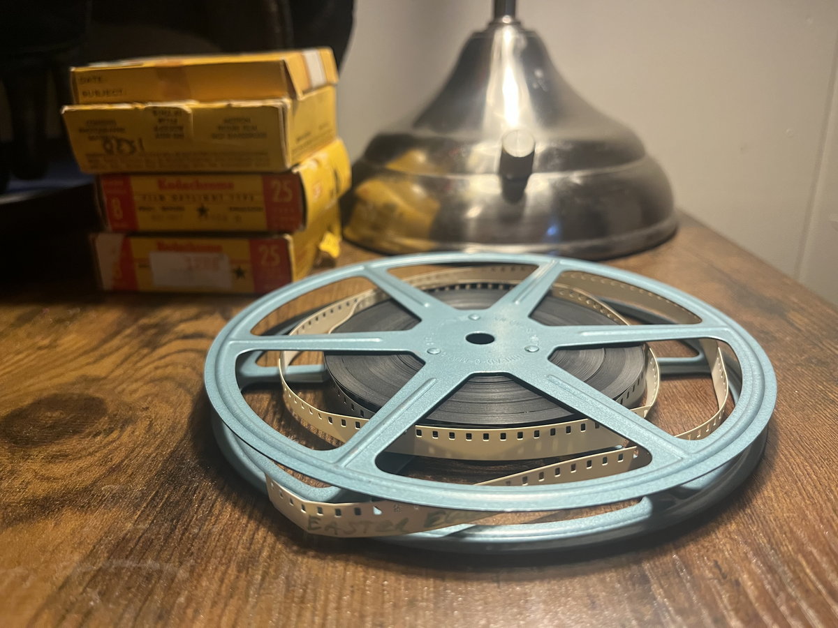 A blue plastic reel of film on a wooden desk beside a stack of yellow processing boxes.