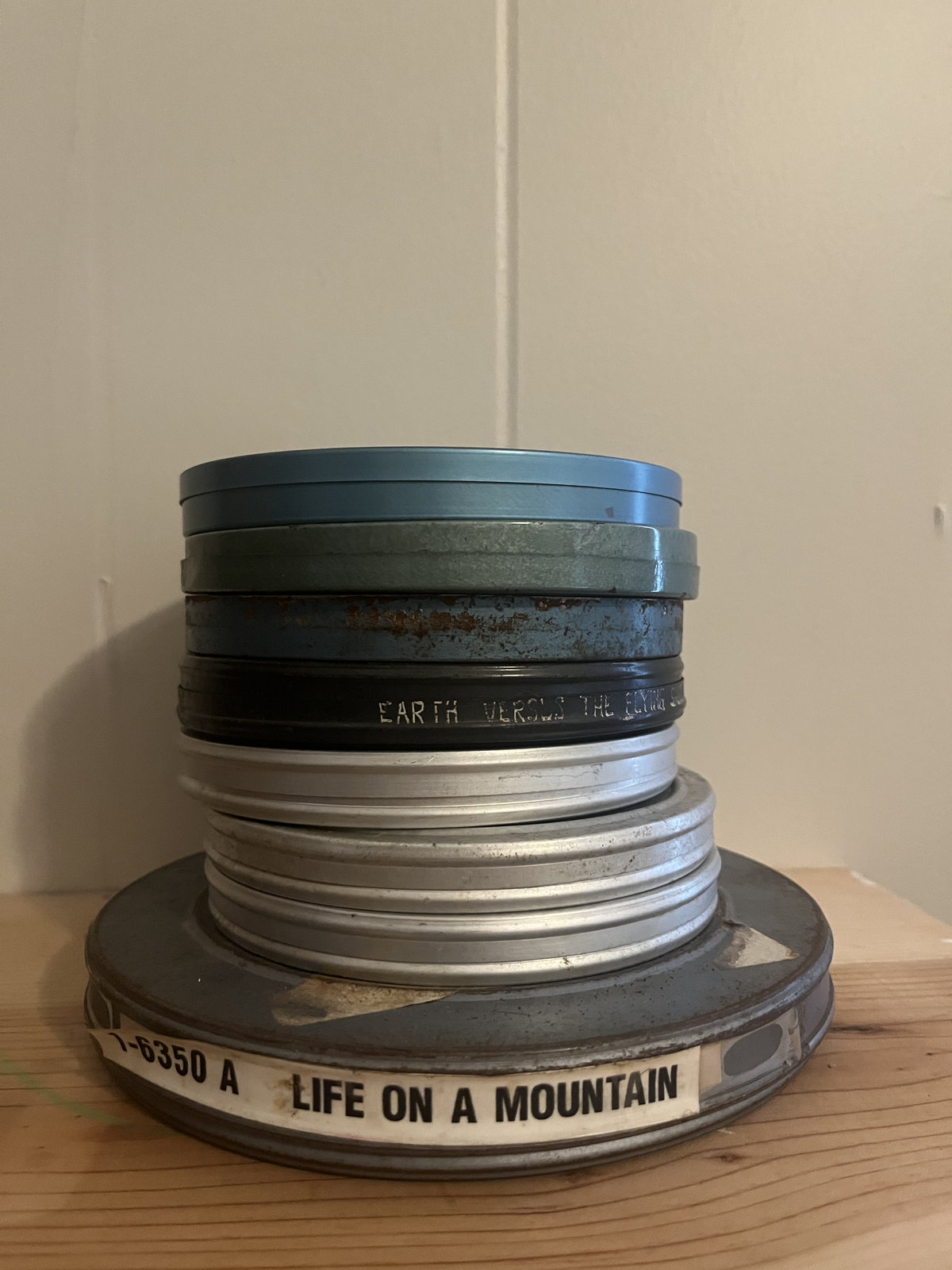 A stack of metal 16mm film cans on a plywood shelf.