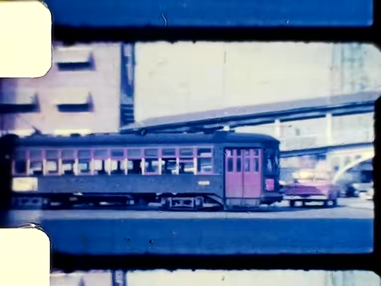 A frame of digitized colour footage: a green streetcar passing a New Orleans building, the film’s sprocket edge visible on the left.